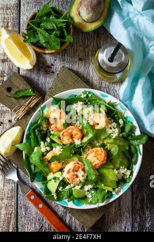 Food dieting concept. Couscous salad with arugula, avocado and grilled shrimps on rustic wooden table. Top view flat lay. Stock Photo
