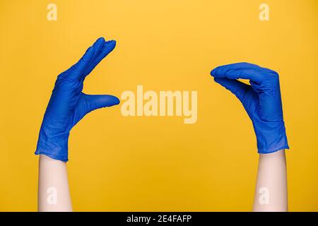 Close up of male showing talking to each other hands, dressed in medical protective blue gloves, isolated on yellow studio background with copy space. Stock Photo