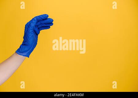 Close up of young woman bending hand fingers fast, wears medical protective gloves, isolated on yellow studio background with copy space Stock Photo