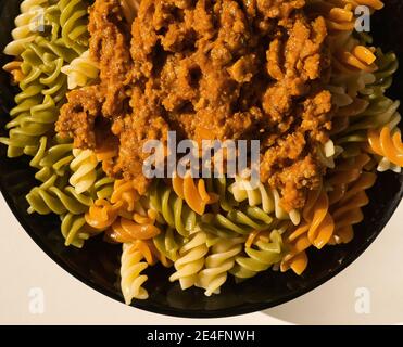 a black plate of fresh italian boiled pasta fusilli with meat served on a withe table, italian food Stock Photo