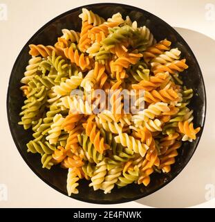 a black plate of fresh italian boiled pasta fusilli served on a withe table, italian food Stock Photo