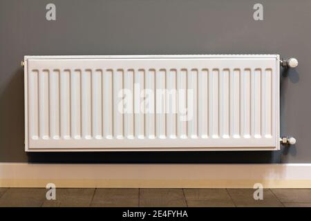 White metal heating radiator mounted on gray wall inside a room. Stock Photo