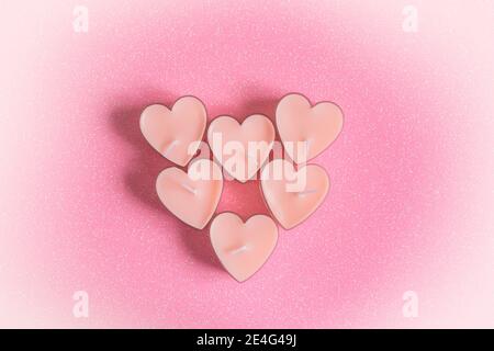 Heart-shaped candles on a pink shiny background. The concept of Valentine's Day, romance, wedding, love. The tender feelings of two hearts. Top view o Stock Photo