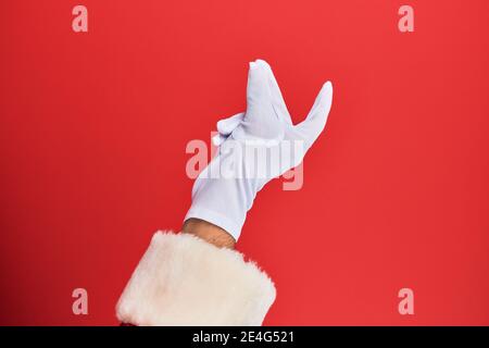 Hand of a man wearing santa claus costume and gloves over red background snapping fingers for success, easy and click symbol gesture with hand Stock Photo