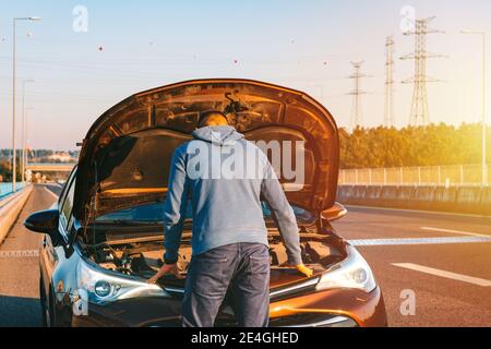 Man with his broken car on the highway roadside. Automobile breaks down on the autobahn. Open the car bonnet, check engine Stock Photo