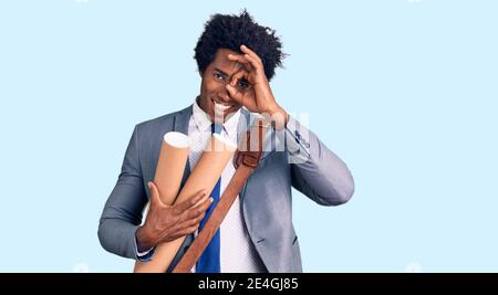 Handsome african american man with afro hair holding paper blueprints smiling happy doing ok sign with hand on eye looking through fingers Stock Photo