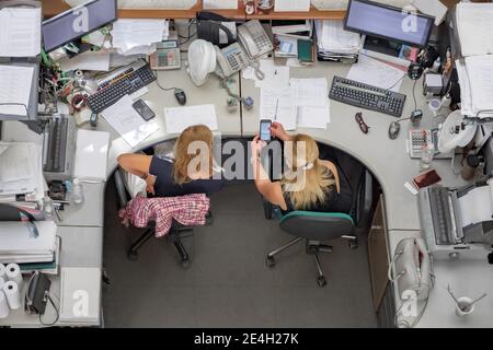 Two woman colleagues using smartphone in the office demonstrate message on cell phone top view. Working days of office manager worker and female Stock Photo