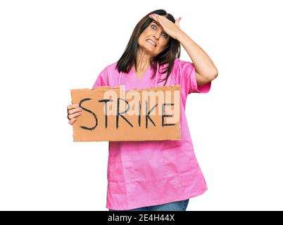 Middle age brunette doctor woman holding strike banner cardboard stressed and frustrated with hand on head, surprised and angry face Stock Photo