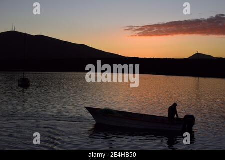 A lone boat and a fisherman silhouetted on San Quintin harbor in Baja California at Molino Viejo, with the sunset in the background Stock Photo