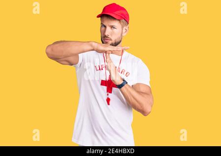 Young caucasian man wearing lifeguard t shirt holding whistle doing time out gesture with hands, frustrated and serious face Stock Photo