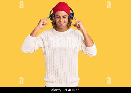Young hispanic man listening to music using headphones covering ears with fingers with annoyed expression for the noise of loud music. deaf concept. Stock Photo