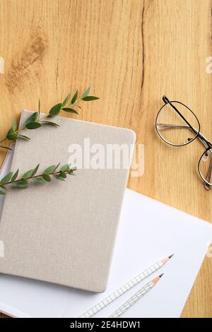 Elegant freelancer workspace with paper notebook, diary, glasses, eucalyptus leaves on wooden table. Home office desk. Top view, flat lay Stock Photo