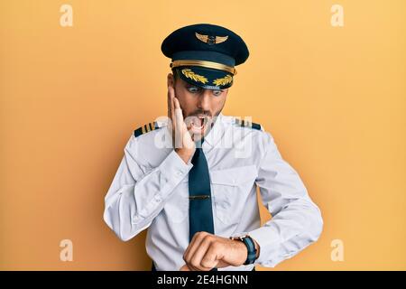 Handsome hispanic man wearing airplane pilot uniform looking at the watch time worried, afraid of getting late Stock Photo