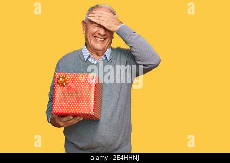 Senior caucasian man holding gift stressed and frustrated with hand on head, surprised and angry face Stock Photo