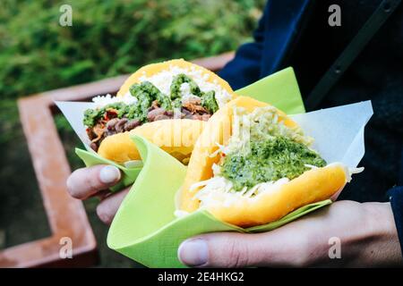 Woman holding two fried Arepas, a typical Venezuelan Street Food with green Salsa, cheese and beans at a Street Food Festival in Dusseldorf, Germany Stock Photo