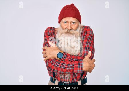 Old senior man with grey hair and long beard wearing hipster look with wool cap shaking and freezing for winter cold with sad and shock expression on Stock Photo