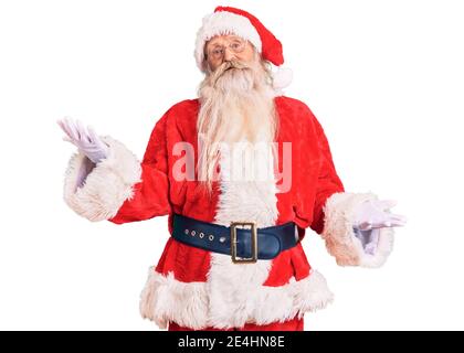 Old senior man with grey hair and long beard wearing traditional santa claus costume smiling cheerful with open arms as friendly welcome, positive and Stock Photo