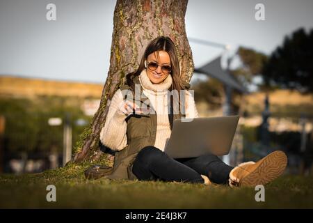 Woman sitting outdoors with credit card and laptop making an online payment Stock Photo