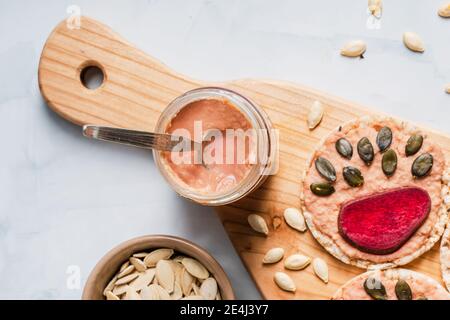 Hummus in jar by Crispy puffed rice cakes on table hummus spread and tomato and beet vegetables and sesame pumpkin seeds on the table - top view on he Stock Photo