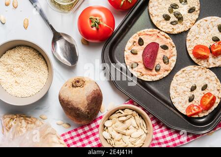 Crispy puffed rice cakes on table hummus spread and tomato and beet vegetables and sesame pumpkin seeds on the table - top view on healthy vegetarian Stock Photo