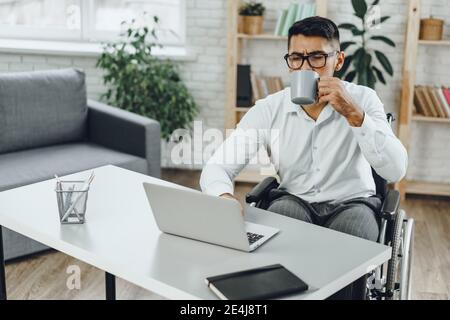 Disabled young businessman drinking coffee at his working table Stock Photo