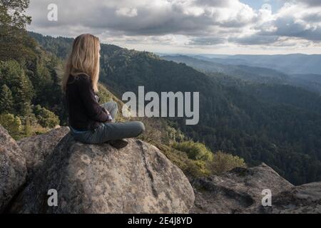 A woman sits looking out over the forested hills and wilderness of the Santa Cruz mountains in California. Stock Photo