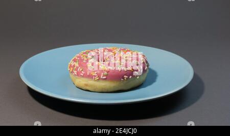 Pink sweet doughnut or donut with colored sprinkles on a blue background. Bitten off American bagel. Stock Photo