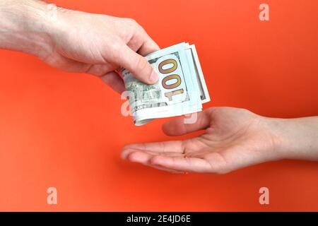 Hand giving folded money usa dollar in other hand on a red background. Bribe concept. Stock Photo