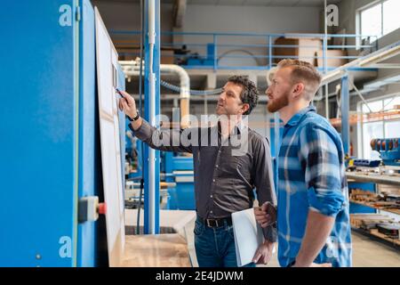 Two carpenters talking over documents in production hall Stock Photo