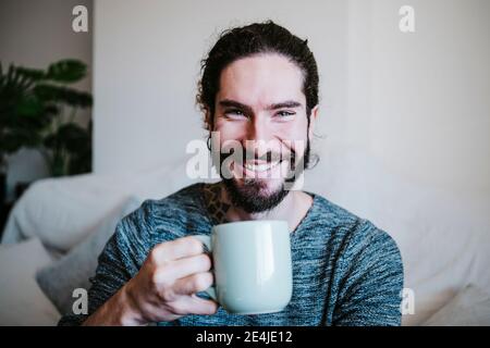 Young man smiling while drinking coffee sitting at home Stock Photo
