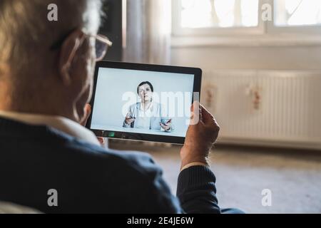 Female doctor consulting male patient on video call through digital tablet at home Stock Photo