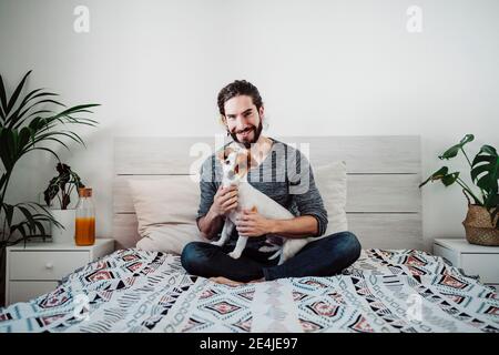 Handsome man sitting with dog on bed at home Stock Photo
