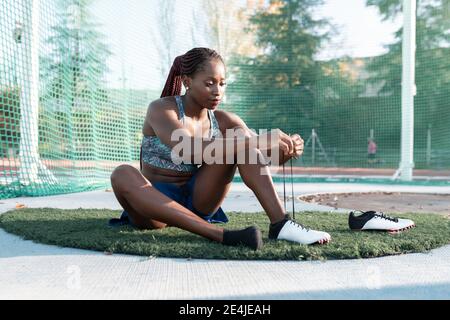 Female athlete tying shoelace against net in sports court Stock Photo