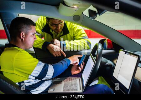 Male technician discussing over mobile phone while programming in electric car Stock Photo