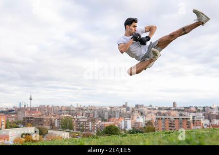 Young male acrobat practicing kickboxing in mid-air on hill in city Stock Photo