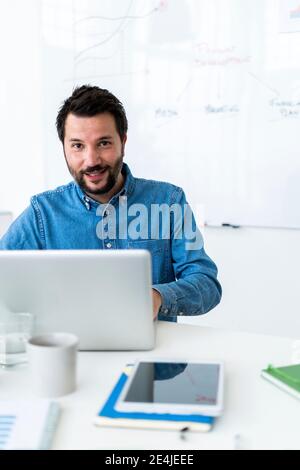 Portrait of smiling man using laptop in office Stock Photo