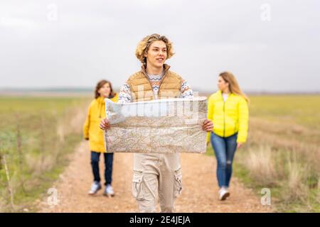 Three siblings hiking with map along dirt road Stock Photo