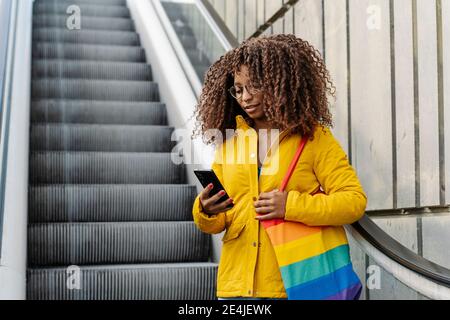 Woman with multi colored purse using mobile phone while standing on escalator in city Stock Photo