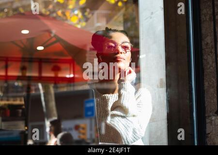 Confident young woman wearing eyeglasses looking through window at cafe Stock Photo
