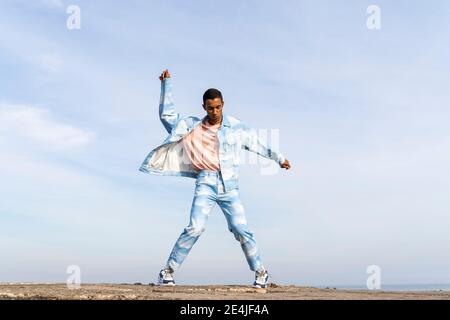 Man wearing denim suit dancing while standing against sky Stock Photo