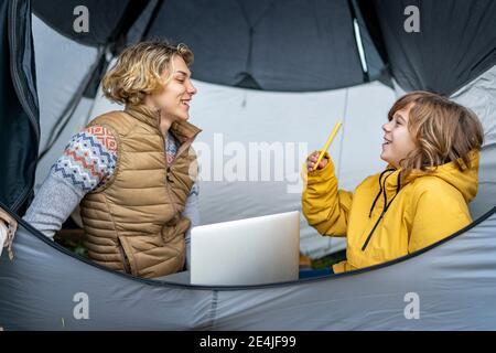 Two brothers camping inside tent with laptop and smart phone Stock Photo