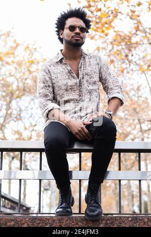 Stylish mid adult man wearing sunglasses sitting on railing Stock Photo