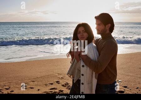 Young man embracing woman while standing against sea Stock Photo