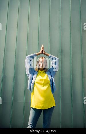 Young woman with hands clasped against wall on sunny day Stock Photo