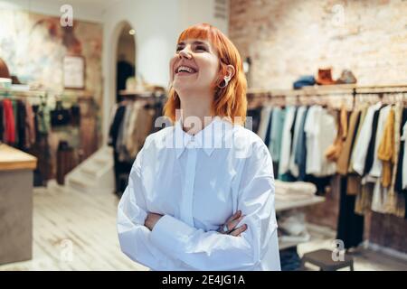 Successful woman standing in her store. Happy female entrepreneur in her fashion retail store looking up and laughing. Stock Photo