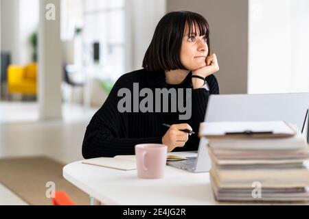 Thoughtful female student with hand on chin studying in study room Stock Photo