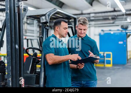 Male colleagues discussing over document while working in factory Stock Photo