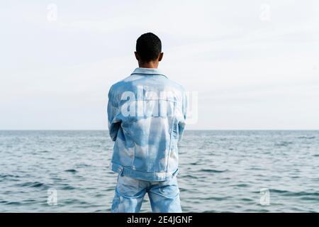 Young man wearing denim suit standing against sea Stock Photo