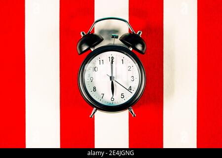 Alarm clock lying on white and red striped pattern Stock Photo