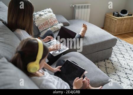 Daughter with digital tablet while mother using laptop at home Stock Photo